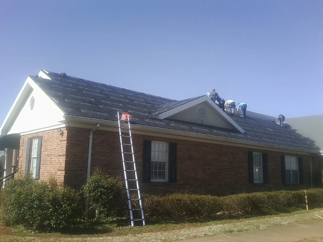 Crew tearing shingles off a brick ranch roof with a ladder set — Emergency Roof Repair work by our crew in Westbrook