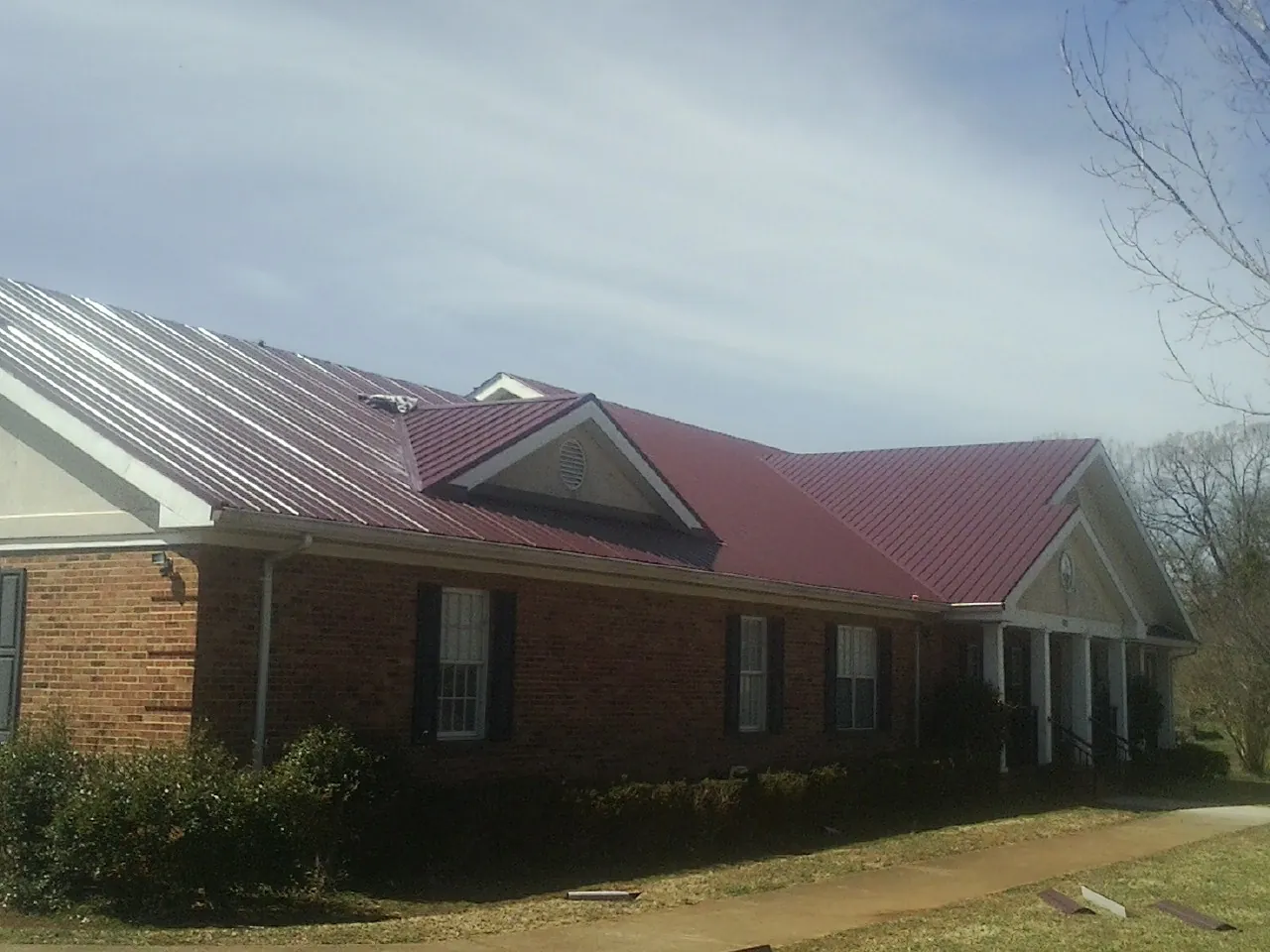 Red metal roof with gabled entries on a long brick building, from a Hail Damage Roof Repair job in Westbrook