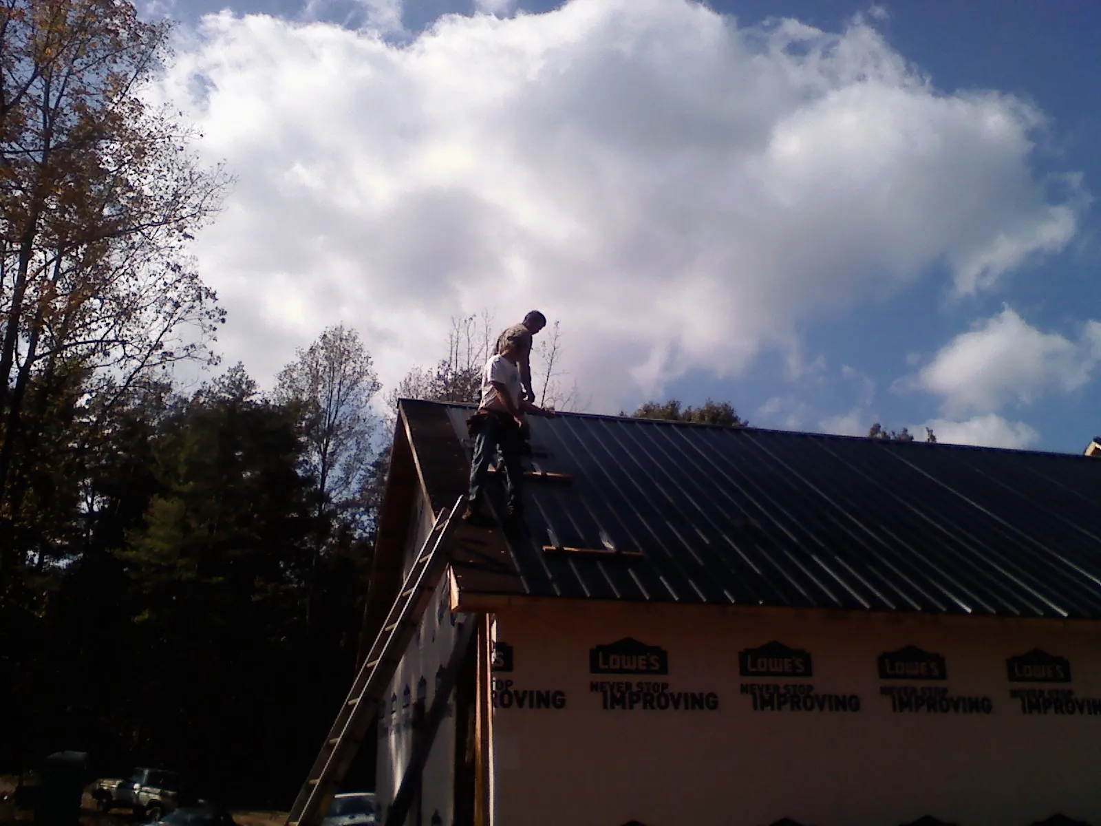 Roofer fastening dark metal panels high against a cloudy sky, from a Roof Inspection job in Westbrook