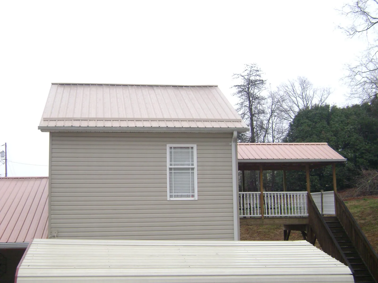 Tan metal roofs on a two story addition and attached porch, from a Roof Replacement job in Westbrook
